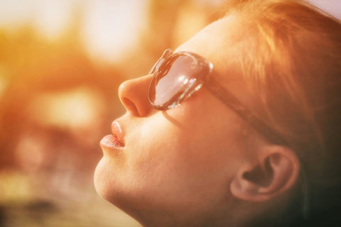 Mujer de perfil tomando el sol, protegiéndose con gafas de sol pero obteniendo los beneficios de la Vitamina D y los ritmos circadianos